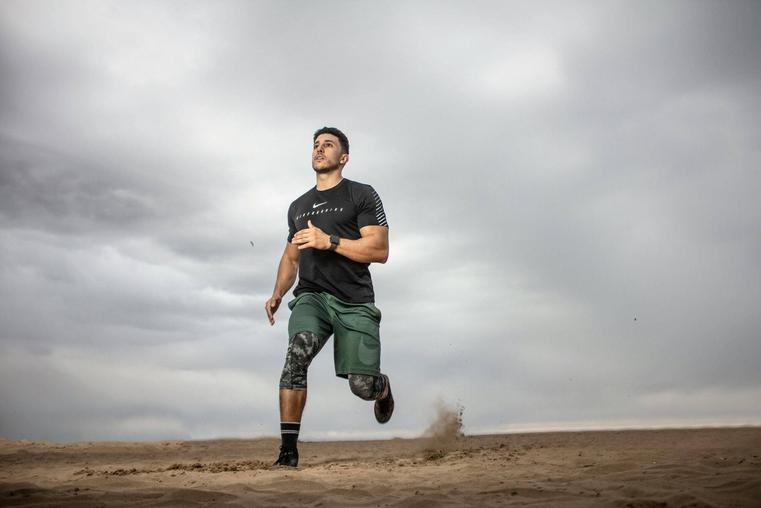 Athlete running on sand under a cloudy sky, representing discipline and physical fitness as foundations for leadership.